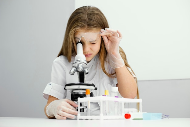 Front view of curious young girl scientist using microscope