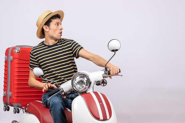 Front view of curious young man with straw hat on moped staring at something