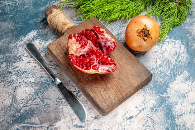 Front view a cut pomegranate on chopping board pomegranate dinner knife on blue-white