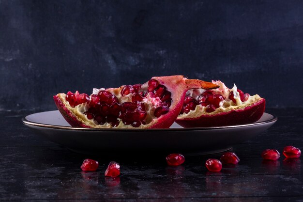 Free photo front view cut pomegranate on a plate  on a black background