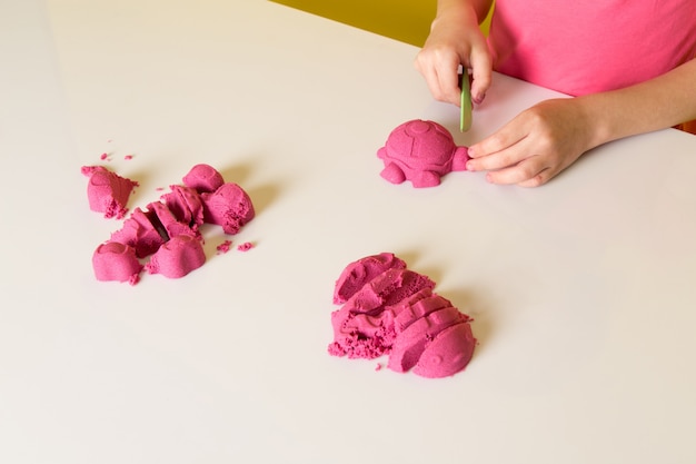 A front view cute adorable boy in pink t-shirt playing with colorful kinetic sand