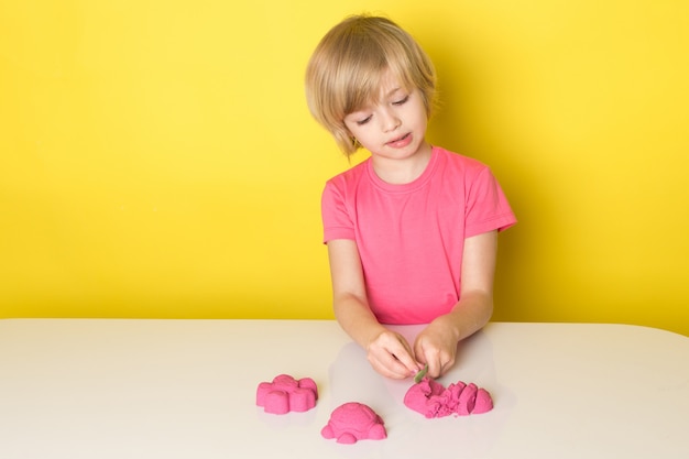 Free photo a front view cute adorable boy in pink t-shirt playing with colorful kinetic sand