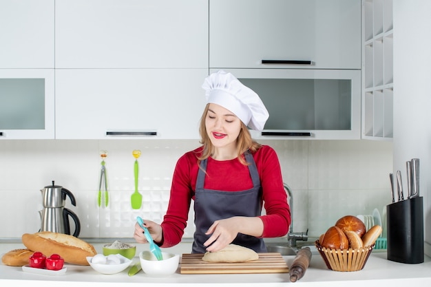 キッチンで料理人の帽子とエプロンバタリングパンの正面図かわいいブロンドの女性