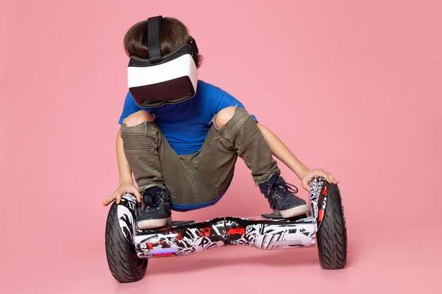 A front view cute boy in blue t-shirt playing vr on segway on the pink space