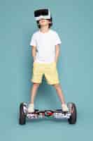 Foto gratuita un ragazzo sveglio di vista frontale che gioca vr sul segway in maglietta bianca sul pavimento blu