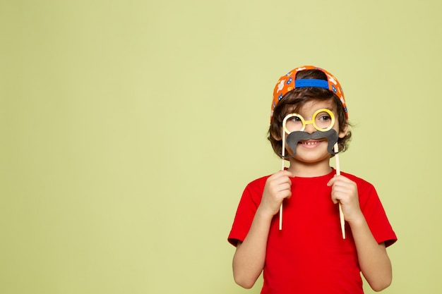 A front view cute boy in red t-shirt and baseball cap on the stone colored space