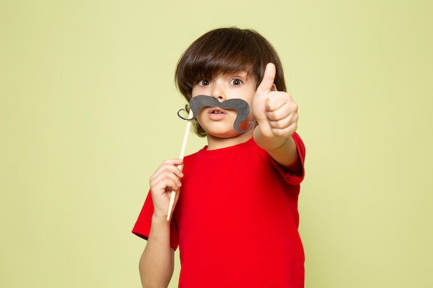 石の色の空間に口ひげを保持している赤いtシャツの正面のかわいい男の子