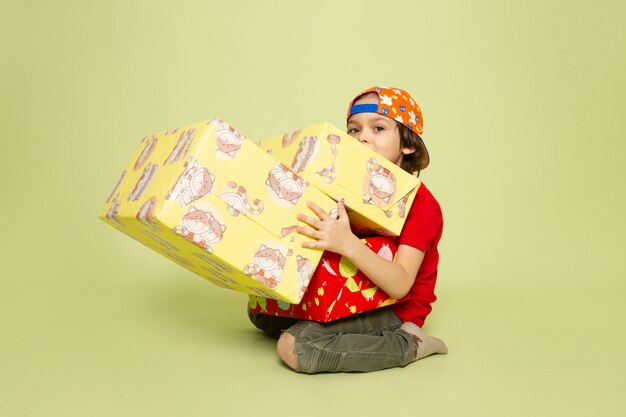 A front view cute boy in red t-shrit holding presents on the stone colored space