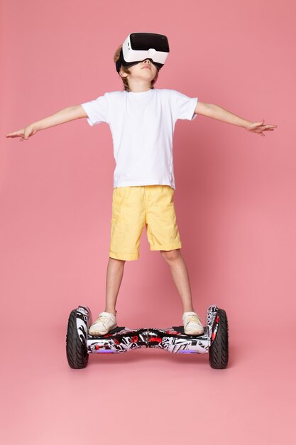 A front view cute boy in white t-shirt and orange shorts riding segway on the pink space