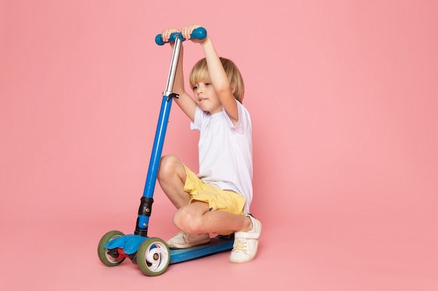 Foto gratuita un ragazzo carino vista frontale in maglietta bianca e jeans gialli in sella a scooter sullo spazio rosa