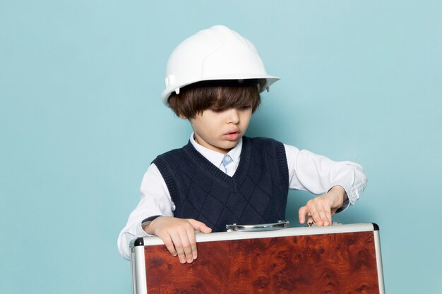 A front view cute business boy in blue classic jamper shirt posing holding brown-silver suitcase business work fashion
