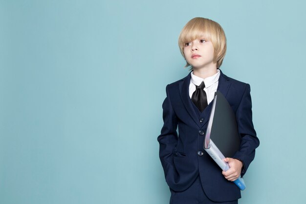 A front view cute business boy in blue classic suit holding black folder business work fashion