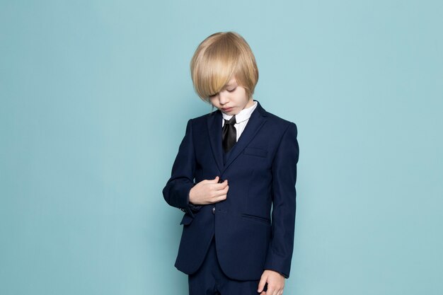 Вид спереди милый деловой мальчик в синем классическом костюме позирует бизнес работа моды