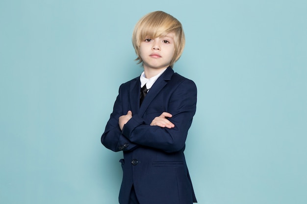 A front view cute business boy in blue classic suit posing looking into the camera business work fashion