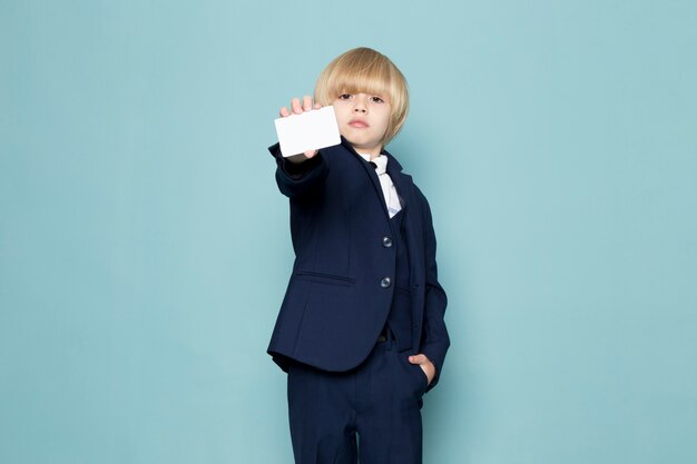 A front view cute business boy in blue classic suit posing showing white card business work fashion