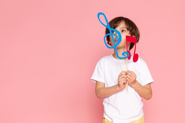 Free photo a front view cute child boy in white t-shirt holding colorful notes on the pink space