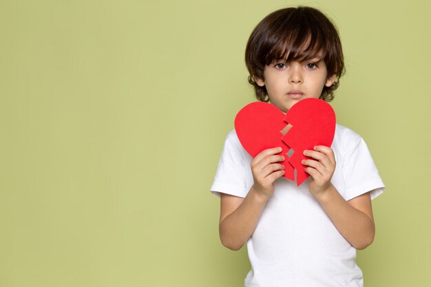 A front view cute child boy in white t-shirt and teared heart shape on the stone colored space