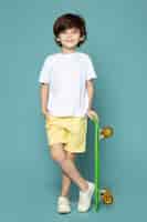 自由面的照片可爱孩子男孩穿着白色t恤和黄色牛仔裤拿着绿色的滑板在蓝色的地板上
