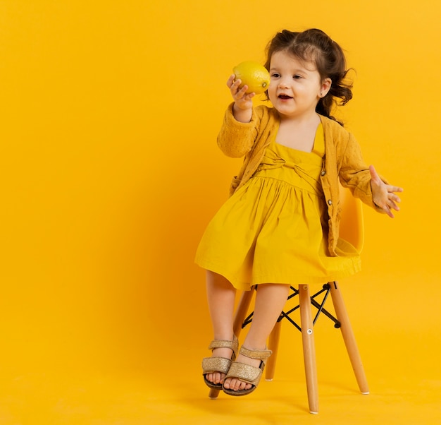 Front view of cute child posing while holding lemon