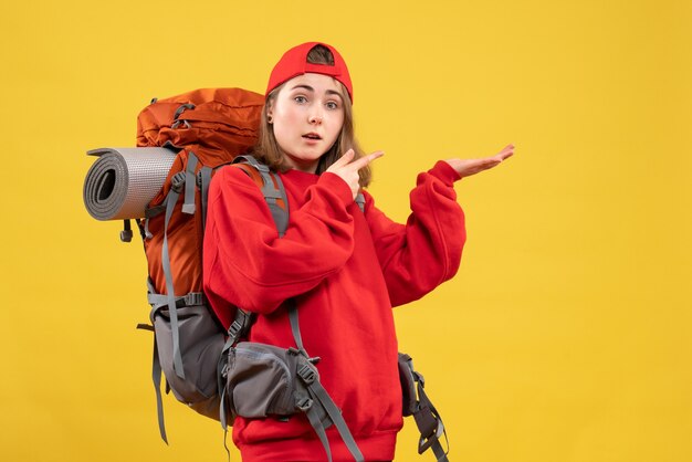 Вид спереди милая женщина-путешественница с рюкзаком, указывая пальцами вправо