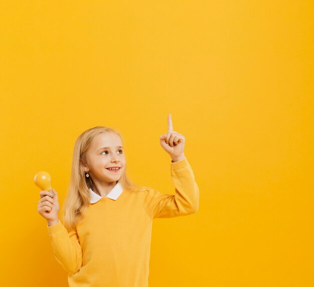 Front view of cute girl posing while holding yellow light bulb and pointing up