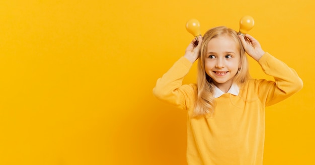 Front view of cute girl posing while holding yellow light bulbs