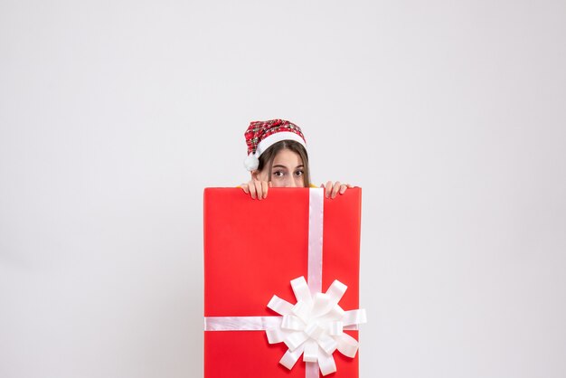 Front view cute girl with santa hat hiding behind big xmas gift