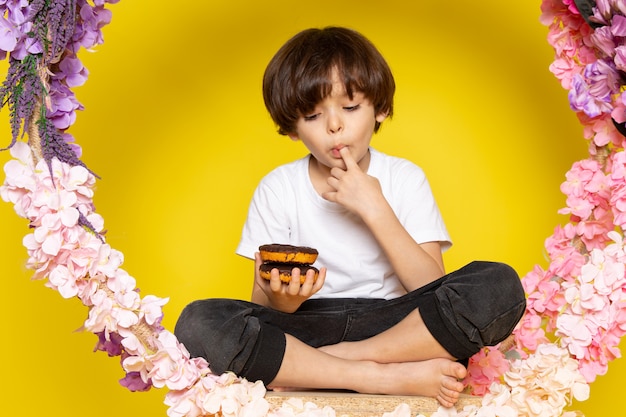 A front view cute kid donuts eating in white t-shirt on the yellow floor