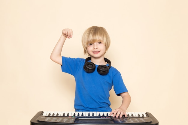 A front view cute little boy smiling in blue t-shirt with black headphones playing little cute piano