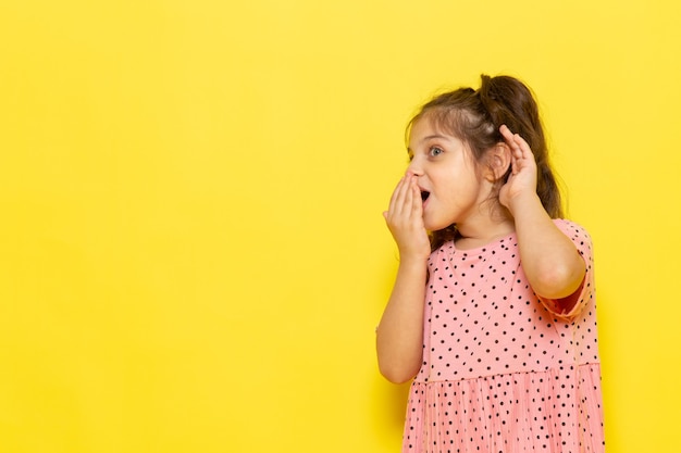 何かをささやくピンクのドレスで正面のかわいい子供