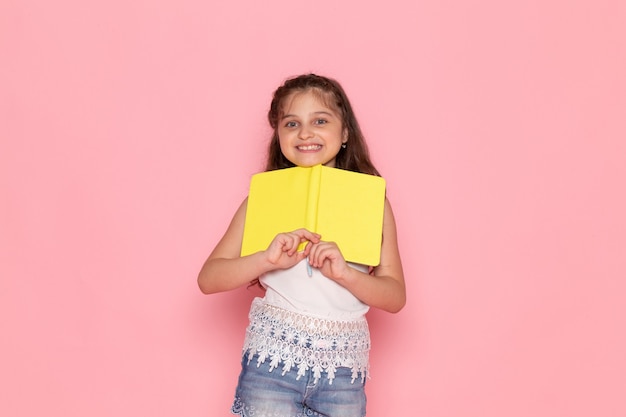Free photo a front view cute little kid smiling and holding yellow copybook