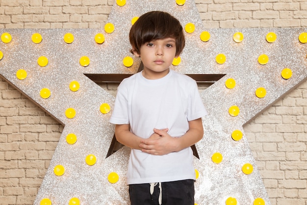 A front view cute little kid in white t-shirt dark jeans on the star designed yellow stand and light background