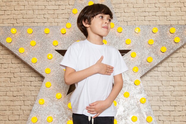 A front view cute little kid in white t-shirt dark jeans on the star designed yellow stand and light background