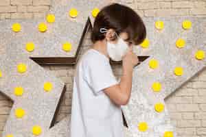 Free photo a front view cute little kid in white t-shirt dark jeans white sterile mask on the star designed yellow stand and light background