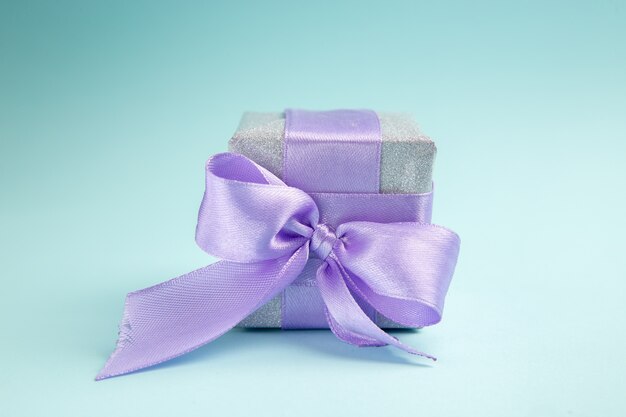 青いテーブルの上の紫色の弓で結ばれた正面図かわいい小さなプレゼント