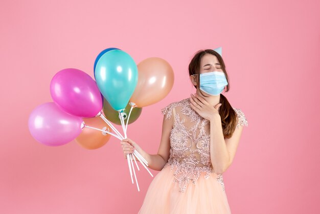 Front view cute party girl with party cap closing eyes holding colorful balloons