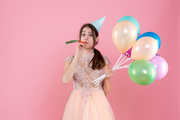 Free photo front view cute party girl with party cap holding balloons using noisemaker