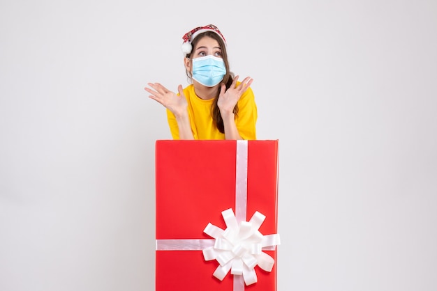 Ragazza di partito carina vista frontale con il cappello della santa che sta dietro il grande regalo di natale