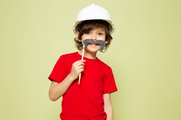 A front view cute smiling boy in red t-shirt and white helmet on the stone colored space