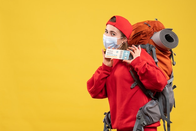 Ragazza carina viaggiatore vista frontale con zaino e maschera tenendo il biglietto