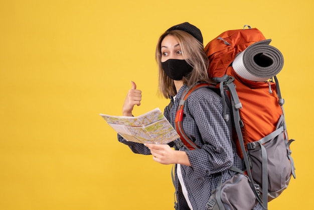 Free photo front view of cute traveler girl with black mask and backpack holding map pointing at behind