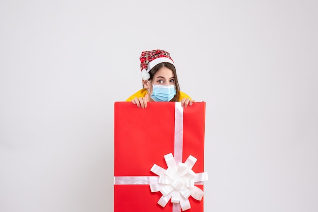 Front view cute xmas girl with santa hat hiding behind big xmas gift