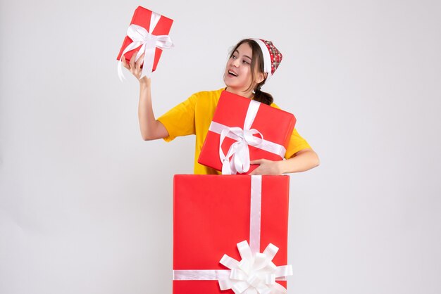 큰 크리스마스 선물 뒤에 서있는 선물을 들고 산타 모자와 전면보기 귀여운 크리스마스 소녀
