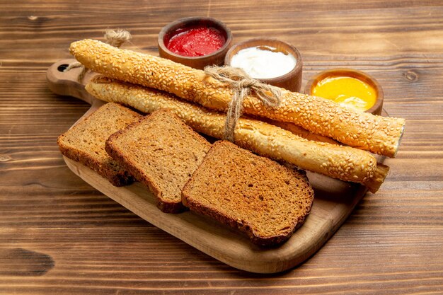 Бесплатное фото Вид спереди темные буханки хлеба с булочками и приправами на коричневом столе еда хлебная булочка острая