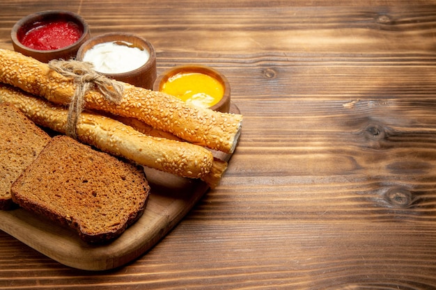 Vista frontale pagnotte di pane scuro con focacce e condimenti su panino di pane marrone da scrivania piccante
