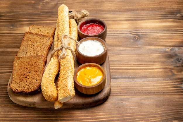 Вид спереди темные буханки хлеба с булочками и приправами на коричневом деревянном столе еда хлебная булочка острая