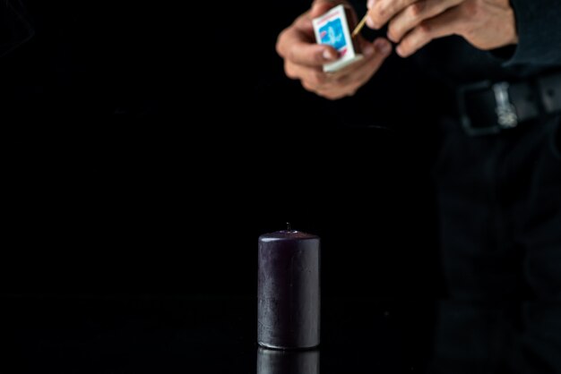 Front view of dark candle getting lighten by male on dark surface