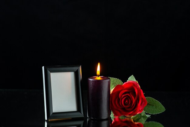 Front view of dark candle with red rose and picture frame on dark surface