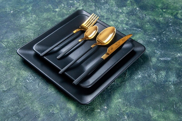 暗い背景に金色のスプーンフォークとナイフで正面図暗いプレート