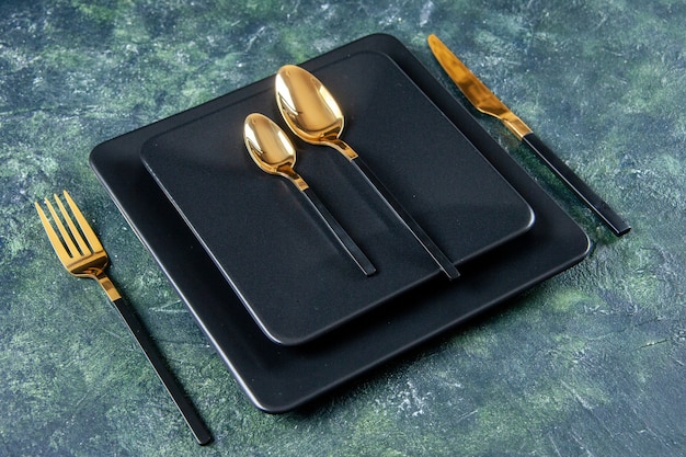 вид спереди темные тарелки с золотыми ложками, вилкой и ножом на темно-синем фоне